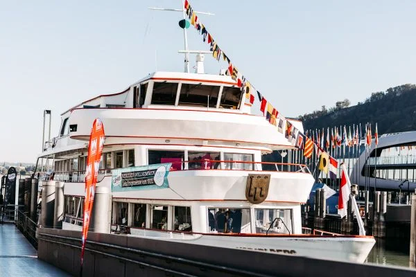 Großes weißes Passagierschiff mit mehreren Decks, am Steg festgemacht und mit bunten Signalfahnen geschmückt.