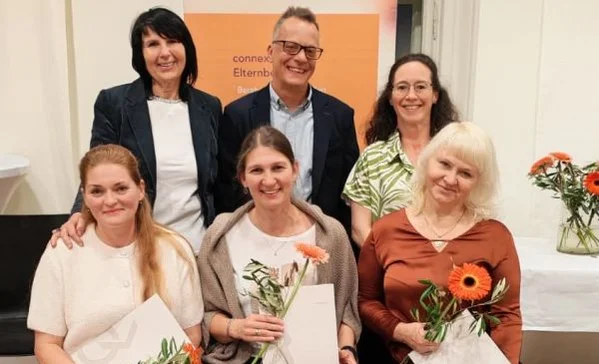 Sechs lächelnde Erwachsene in einem Gruppenfoto; drei sitzen vorne mit Blumen und Urkunden, drei stehen dahinter.