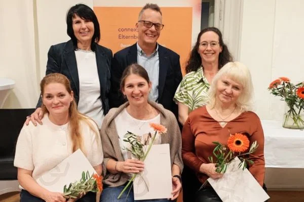 Sechs lächelnde Erwachsene in einem Gruppenfoto; drei sitzen vorne mit Blumen und Urkunden, drei stehen dahinter.